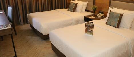 Habitación de hotel con dos camas, piso de madera, una mesita de noche con un teléfono y una revista sobre la cama.