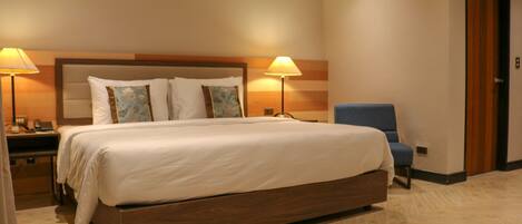 A hotel room with a large bed, two bedside lamps, a wooden headboard, and a blue chair.