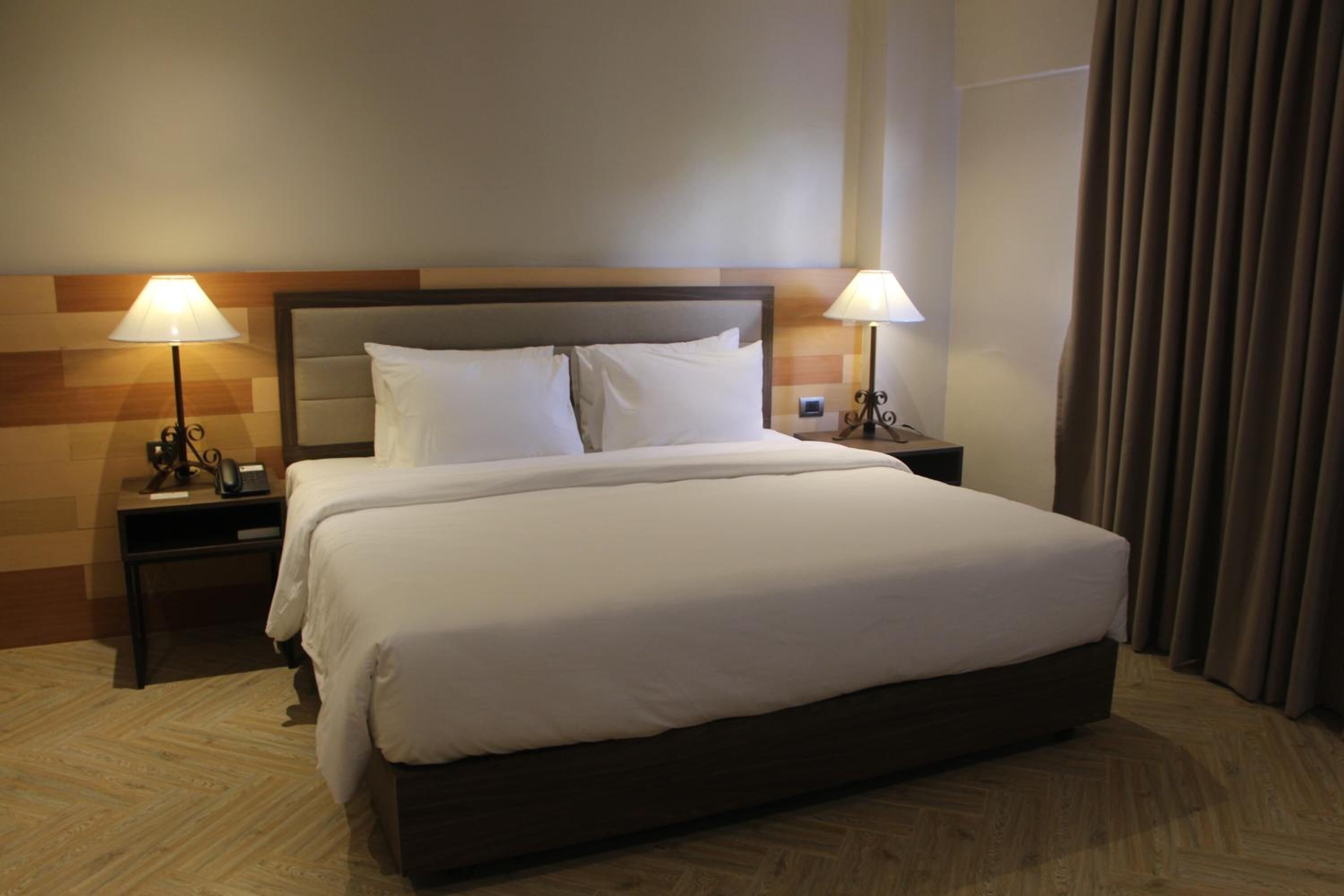 Habitación de hotel con una cama grande, dos lámparas de noche, un cabecero de madera y una cortina en la ventana.