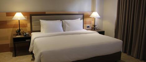 A hotel room with a large bed, two bedside lamps, a wooden headboard, and a curtain on the window.