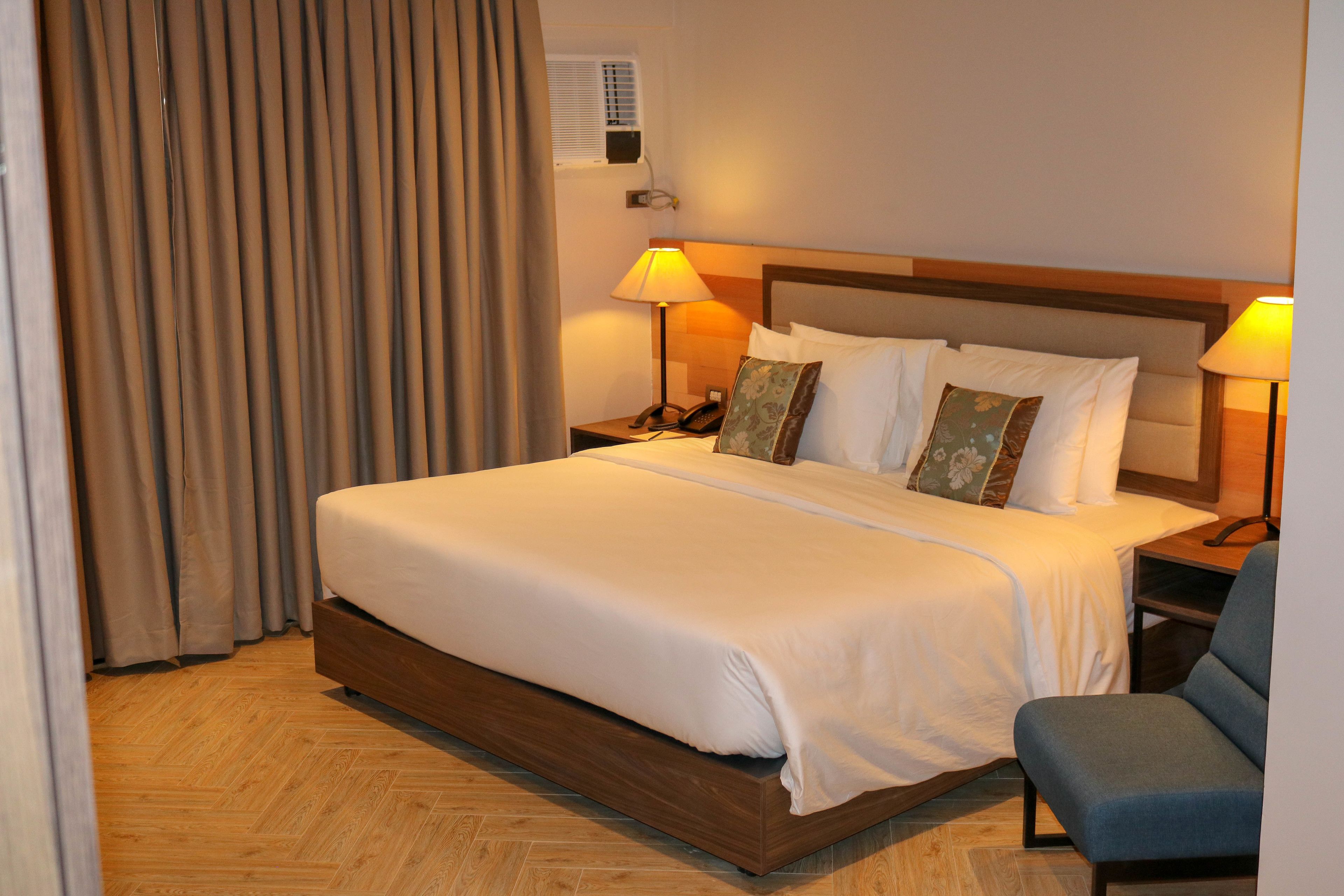 Habitación de hotel con una cama grande, dos mesitas de noche con lámparas, una silla y una ventana con cortinas.