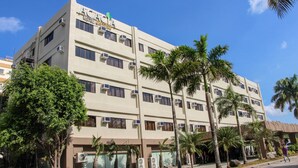 Un hotel de varios pisos con fachada plana, unidades de aire acondicionado y palmeras en primer plano.