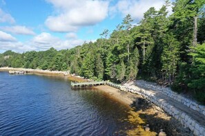 A serene lakeside view with a dock extending into the water, surrounded by dense forest and a stone embankment.