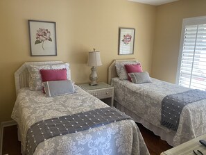 A hotel room with two beds, each with floral-patterned bedding, a bedside table with a lamp, and framed floral artwork on the wall.