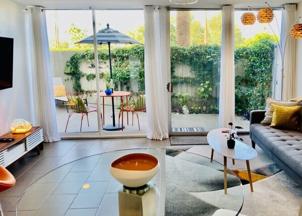 A modern living room with a large glass door leading to an outdoor patio.