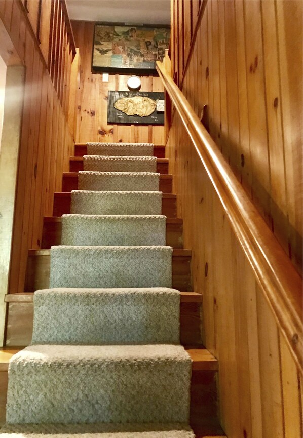Stairs lead to an upper level, flanked by paneling and topped with a framed picture.