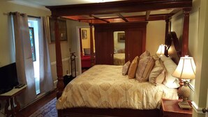 Un lit à baldaquin avec une couvre-lit à motifs, une lampe de chevet et un téléviseur posé sur un meuble en bois.