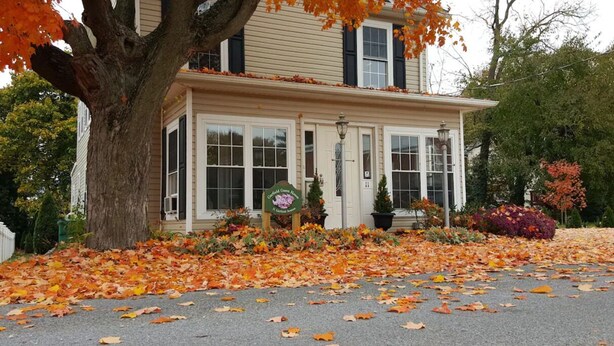 Une maison à deux  étages avec un porche, entourée de feuilles d’automne.