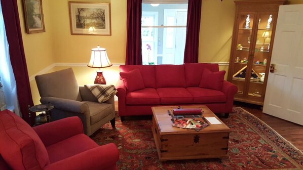 Ein Wohnzimmer mit einem roten Sofa, einem grauen Sessel, einem Holztisch mit Zeitschriften, einer Lampe und einem gemusterten Teppich.