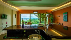 A modern kitchen with a large island, a view of the ocean, and a dining area with a plant and artwork. - LARGE BEAUTIFUL CONDO SUITE 2B/2B IN LAKE ARENAL (Tilaran)