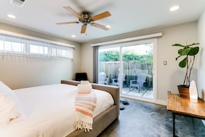 A bedroom with a bed, a ceiling fan, a sliding glass door to a patio, and a potted plant.