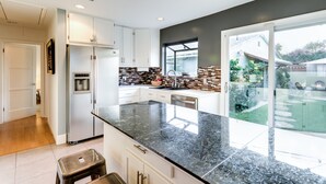 Una cocina moderna con una isla grande, armarios blancos y vistas al jardín trasero.