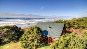 Una casa costera con techo de metal, rodeada de árboles verdes y frondosos, con vista al océano.