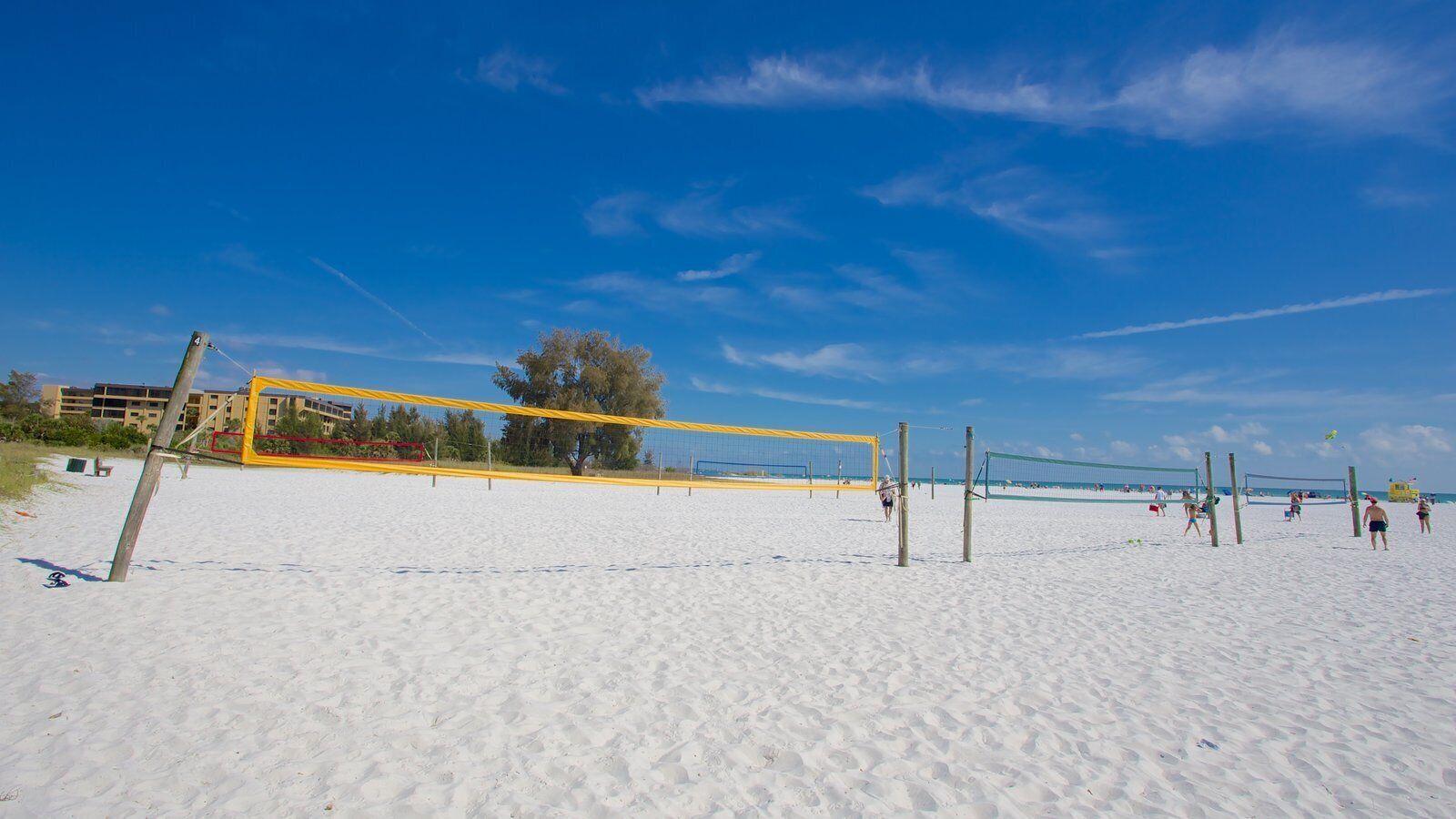 A beach volleyball court with a net, sand, and a few players.