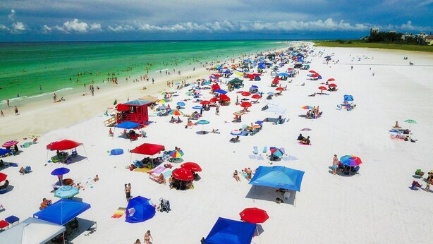 A crowded beach with numerous umbrellas and beachgoers.