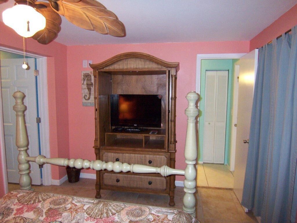 Un dormitorio con una cama, televisión, cabecera de madera y ventilador de techo.