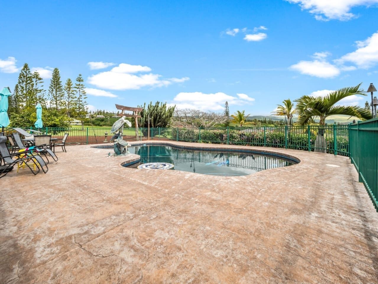 A swimming pool with a curved edge, surrounded by a green fence and palm trees.