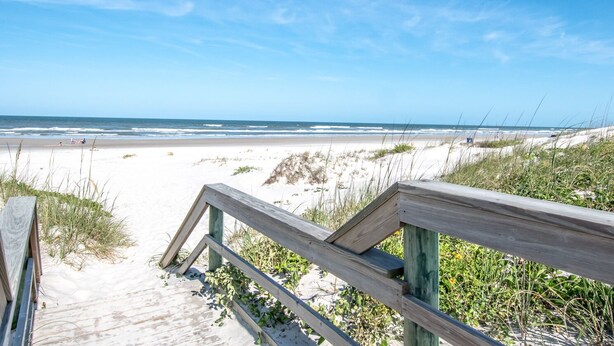 Une promenade en bois qui mène à une plage de sable et offre une vue sur l’océan.