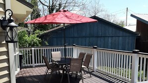A wooden deck with a table and chairs, a red umbrella, and a white fence.