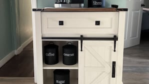 A kitchen island with a coffee maker, a container labeled 'filters', and three black containers labeled 'coffee', 'cream', and 'sugar'.