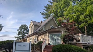 A two-story house with a porch and a sign that reads "The Nest".