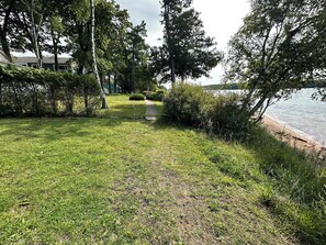 A grassy pathway leading to a lake with trees and shrubs on either side.