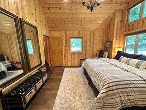 Ein Schlafzimmer einer Holzhütte mit einem großen Bett, einem Spiegel, einem Fenster und einer Chandelier.