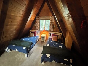 A cozy attic bedroom with two beds, a nightstand, and a window with curtains.