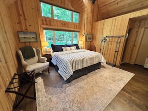 Ein Schlafzimmer mit Bett, Sessel, Nachttisch, Fenster und Tür.