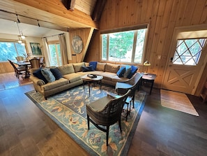 A cozy living room with a sectional sofa, a dining area, and large windows. - Walloon Village Home- Few Steps To Lake Access! (Walloon Village)