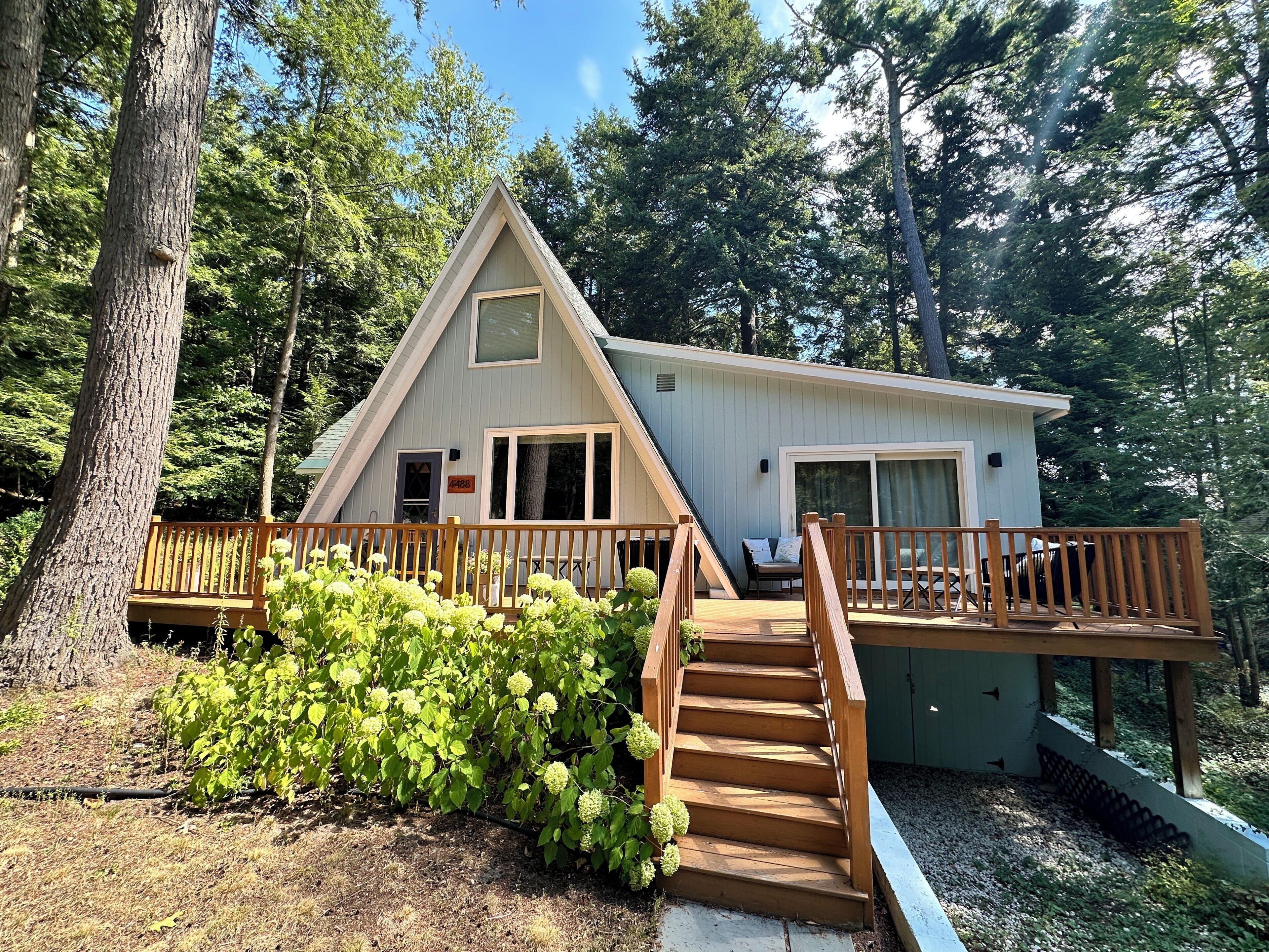 A cabin with a wooden deck, a staircase, and a view of the surrounding forest.