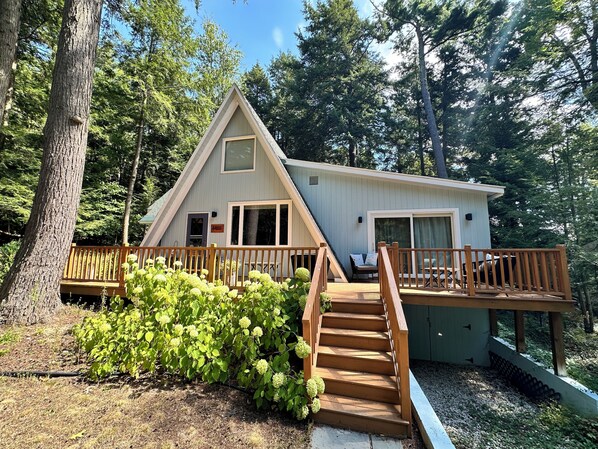 A cabin with a wooden deck, a staircase, and a view of the surrounding forest.