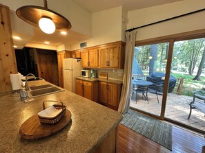 A kitchen with wooden cabinets, a built-in microwave, and a large window leading to an outdoor patio. - Walloon Village Home- Few Steps To Lake Access! (Walloon Village)