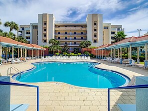 A swimming pool with lounge chairs and umbrellas, surrounded by a multi-story building with balconies. - Relax near the pond in this gorgeous condo. Ow15-504 (New Smyrna Beach)