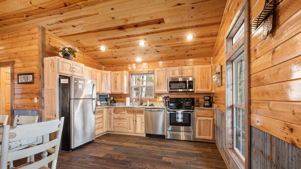 A wooden cabin kitchen with a refrigerator, microwave, oven, and sink.