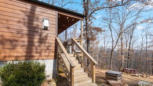 A wooden cabin with a covered porch, a staircase leading to the entrance, and a picnic table in the yard.