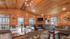 A wooden cabin interior with a dining table, chairs, a sofa, and a television mounted on the wall.