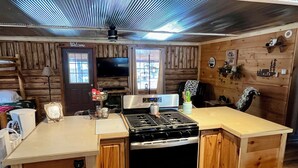 A rustic kitchen with wooden cabinets, a stove, and a television. - Bear Den Log Cabin (Wetmore)