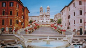 Una imponente escalera conduce a una iglesia con un campanario, rodeada de escalones decorados con flores y una fuente central.