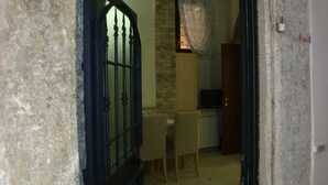 Una habitación con pared de piedra, puerta de madera, una mesa de comedor con sillas y un televisor.