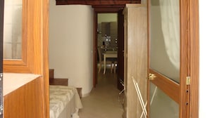 Un pasillo estrecho con una puerta de madera a la derecha, una mesita con sillas y un televisor sobre un estante encima de la puerta.