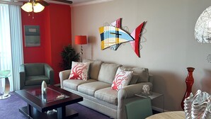 Ein Wohnzimmer mit einer Couch, einem Couchtisch und Sesseln, einem Deckenventilator und einer Wanddekoration mit Fischmotiven.