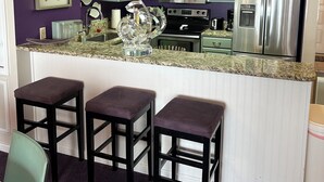 Eine Küche mit taubenblauen Schränken, einer Granitabdeckung, einem Edelstahlkühlschrank und einer Bar mit Hockern.