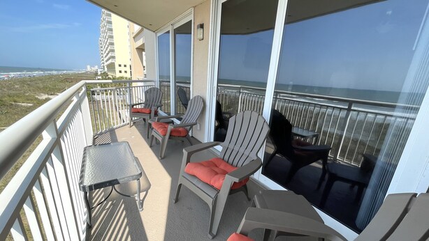 Ein Balkon mit Sitzgelegenheit im Freien, einem Tisch und Blick auf Strand und Meer.