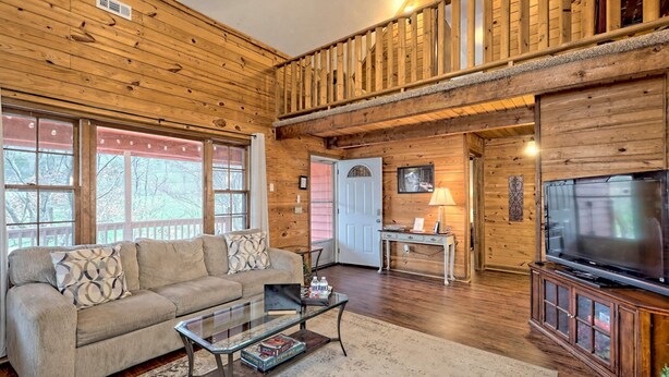A cozy log cabin interior with a sofa, coffee table, TV, and a staircase.