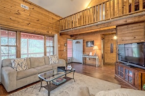 A cozy log cabin interior with a sofa, coffee table, TV, and a staircase. - Little Red House. A charming cabin in Clayton, Ga (Clayton)