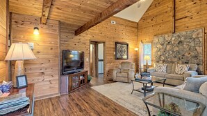 A cozy log cabin interior with a television, comfortable seating, and a stone accent wall.