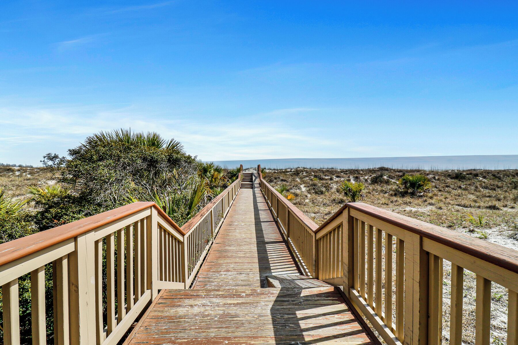 A wooden boardwalk leading to a beach with a clear view of the ocean.