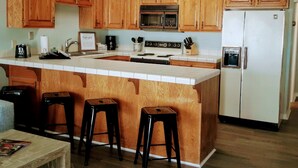 Eine Küche mit Holzausstattung, einer zentralen Kochinsel mit Hockern, einem Kühlschrank und einer Mikrowelle.