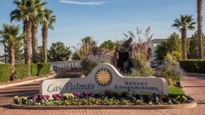 Schild für die Las Palmas Resort Condominiums mit Sonnensymbol, umgeben von Palmen und einem angelegten Garten.